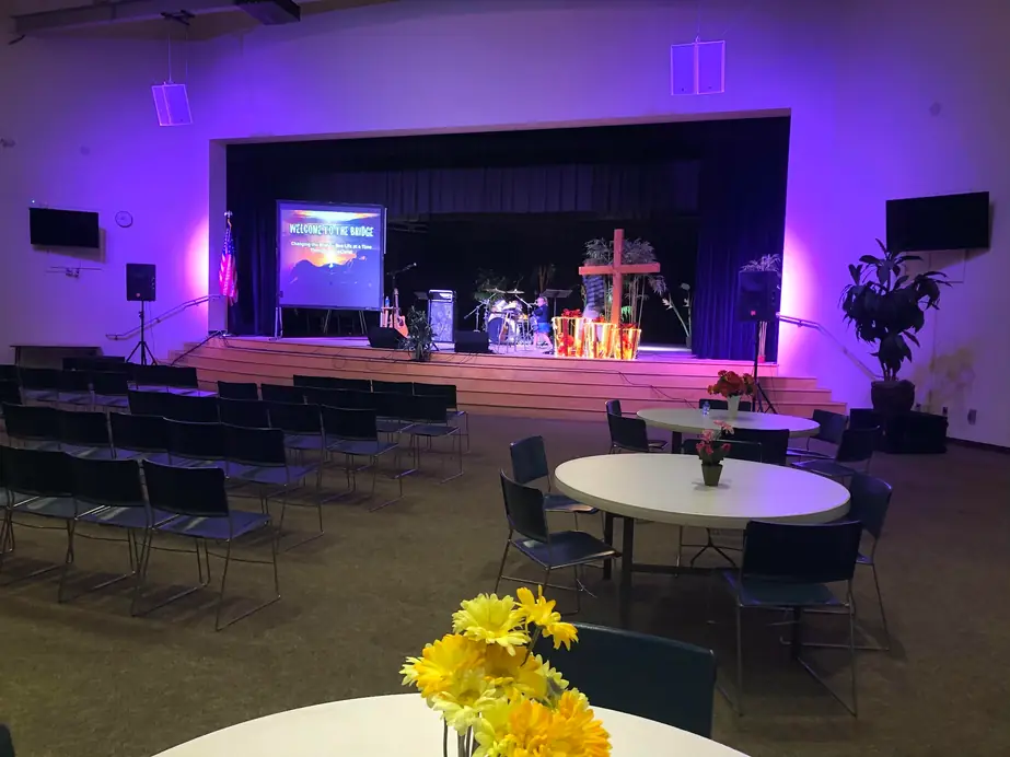 The empty stage in the clubhouse hall, lit and ready, with a cross and daisies on the tables