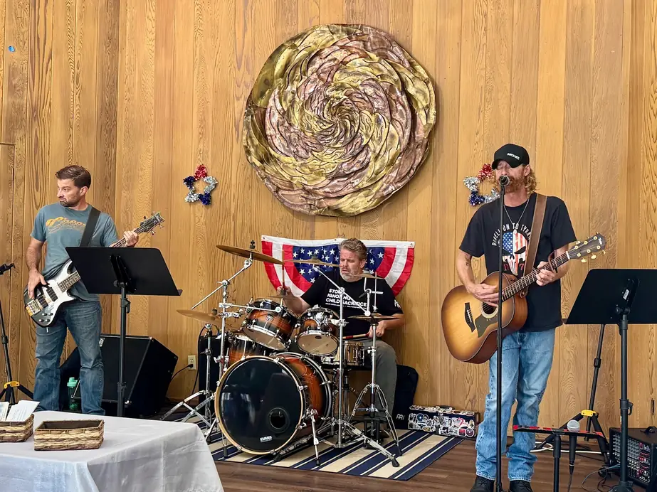 The Bridge Church worship band playing bass, drums and acoustic guitar under the gold swirl on the cedar wall