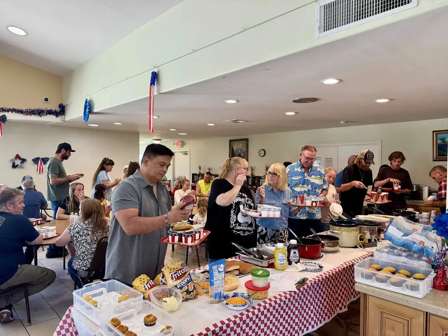 Church family serving each other at a long fellowship lunch table in the clubhouse