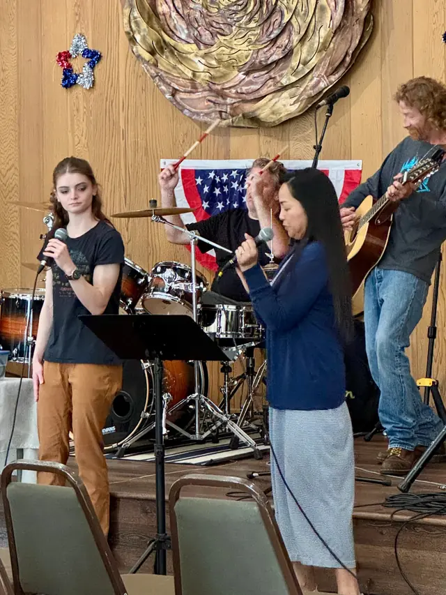 The worship team mid-song, a teen vocalist and a guitarist under flag bunting in the clubhouse hall