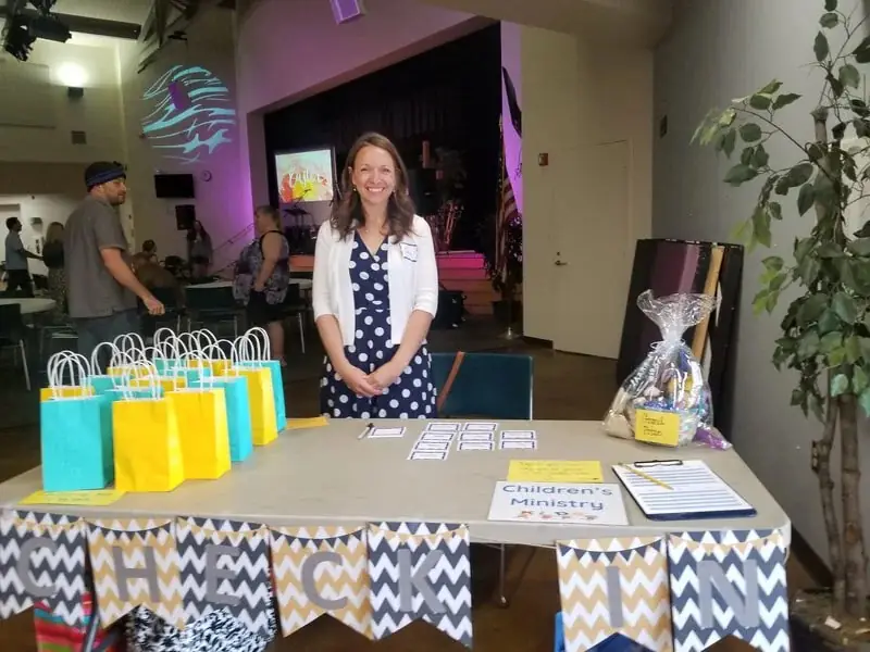 Children's Ministry check-in table with gift bags and a smiling volunteer